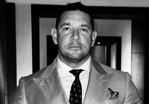 A black and white headshot of Peter Miles, wearing a suit.